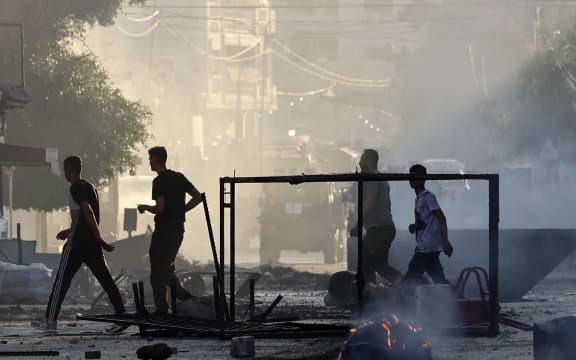 Palestinians walk past burned waste during an Israeli military operation in the Jenin refugee camp in the occupied West Bank on July 3, 2023. Israel has stepped up operations in the northern West Bank, home to Jenin city and its adjacent refugee camp, a stronghold of Palestinian armed groups where there has been a spate of attacks on Israelis as well as attacks by Jewish settlers on Palestinian communities. (Photo by Jaafar ASHTIYEH / AFP)