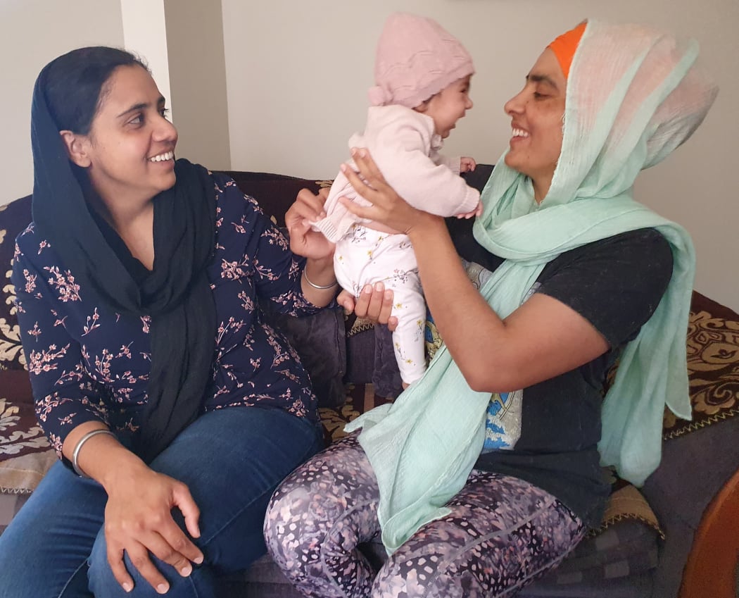 A photo of two women on a couch playing with a three month old baby