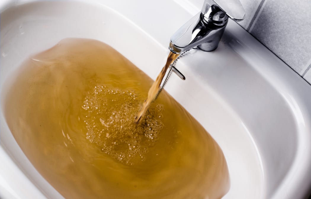 Dirty brown water running into a white sink. Looks very unhealthy,