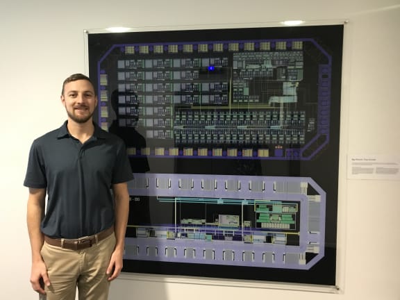 Robert Gallichan stands next to a blown up image of the electronic circuit he has designed to go in the sensor.