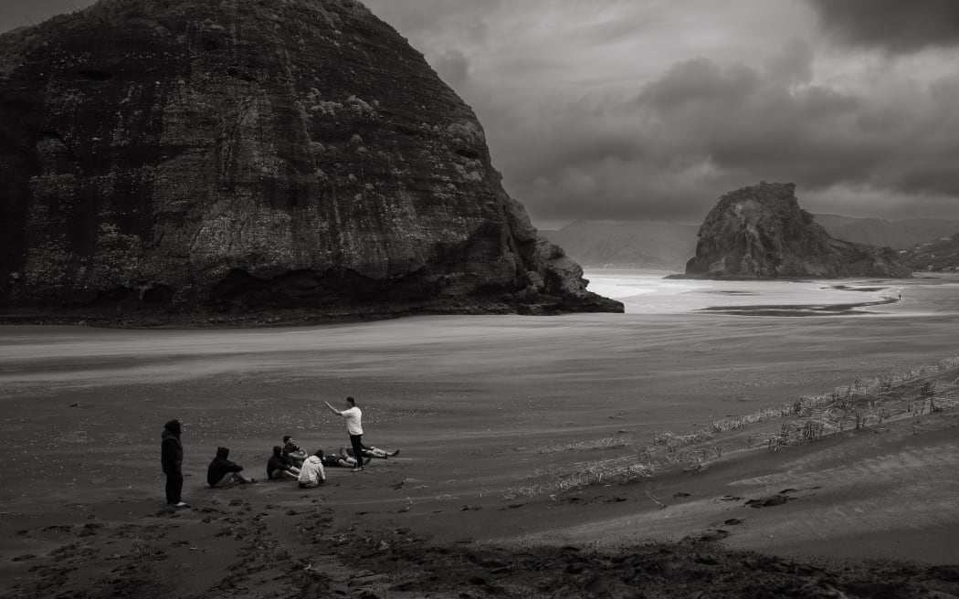 A group of people sit on a beach in a circle listening to a high performance coach.