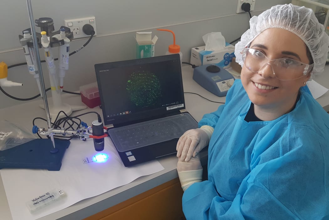 ESR researcher Alicia Haines with a handheld microscope connected to a computer showing an image of fluorescent DNA in a fingerprint.