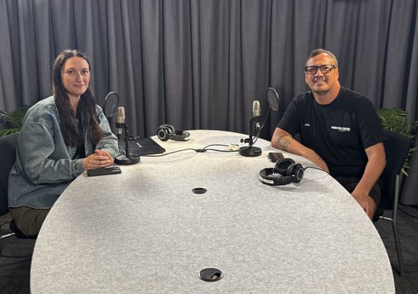 Kara Rickard and Tammy Davis sit facing each other around a round white table as they turn to the camera and smile.