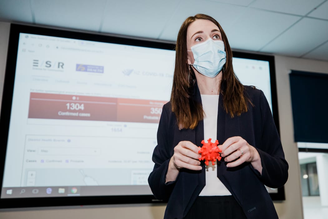 Prime Minister Jacinda Ardern wears a mask and holds a 3D model of the coronavirus during a visit to ESR in Porirua on 20 August 2020.