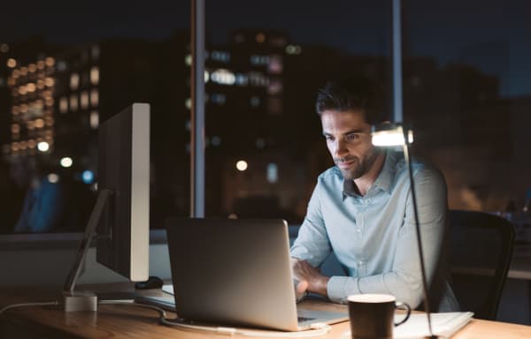 Young businessman working at his desk in an office late at night with city lights glowing in the background