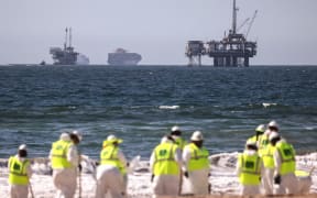 HUNTINGTON BEACH, CALIFORNIA - OCTOBER 09: Cleanup workers search for contaminated sand and seaweed in front of drilling platforms and container ships about one week after an oil spill from an offshore oil platform on October 9, 2021 in Huntington Beach, California. The heavy crude oil spill affected close to 25 miles of coastline in Orange County. Huntington Beach is open but the public is not allowed to enter the water.   Mario Tama/Getty Images/AFP (Photo by MARIO TAMA / GETTY IMAGES NORTH AMERICA / Getty Images via AFP)