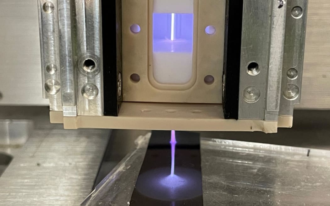 A machine ejects a jet of glowing purple plasma