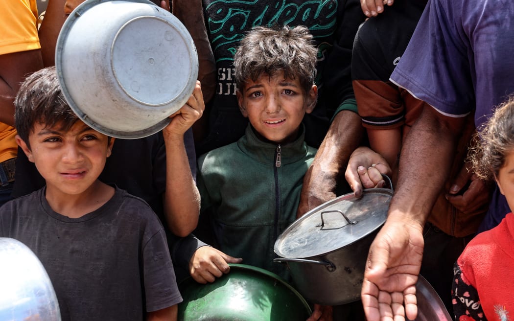 Palestinian children wait in front of a food distribution truck at a displacement camp near Gaza City's port on 22 May, 2025. The Israeli army issued an evacuation warning on May 22 for 14 neighbourhoods of northern Gaza, as it pressed a renewed offensive that has drawn international condemnation.