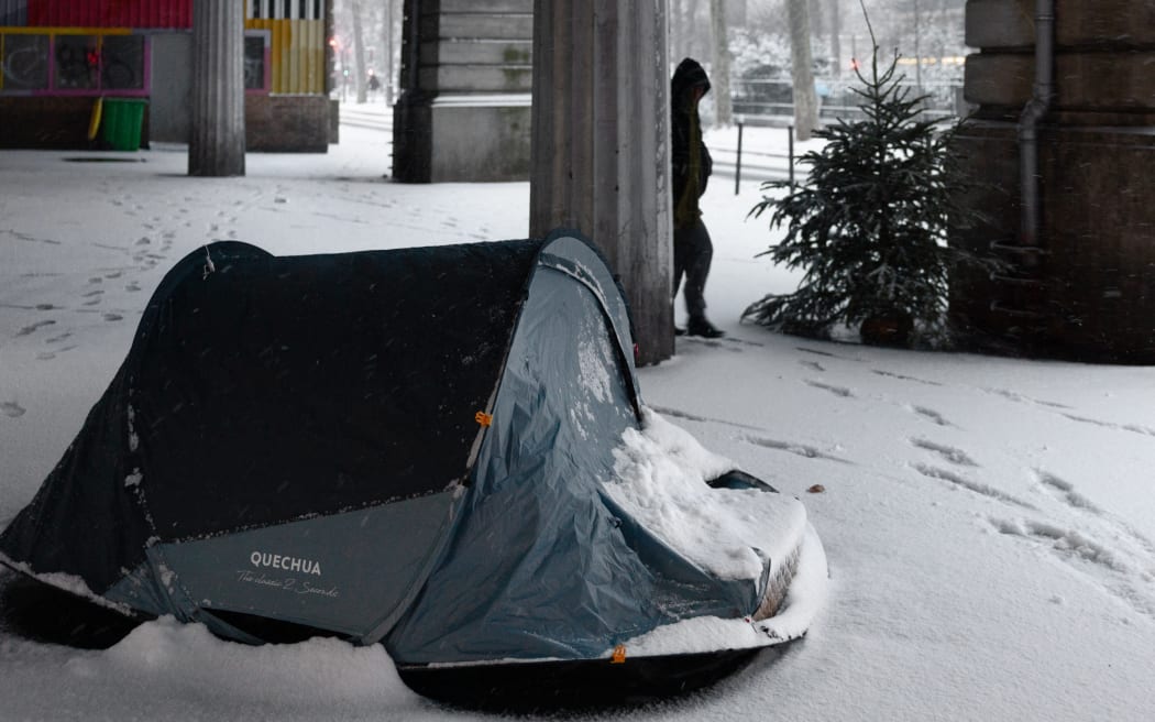 A homeless person's tent is pictured on a snow covered street in Paris on January 7, 2026. Snow and ice are affecting northern and western France, a phenomenon of “rare magnitude in the current climate” according to Meteo-France, which is expected to cause significant restrictions on roads and air transport. (Photo by JOEL SAGET / AFP)