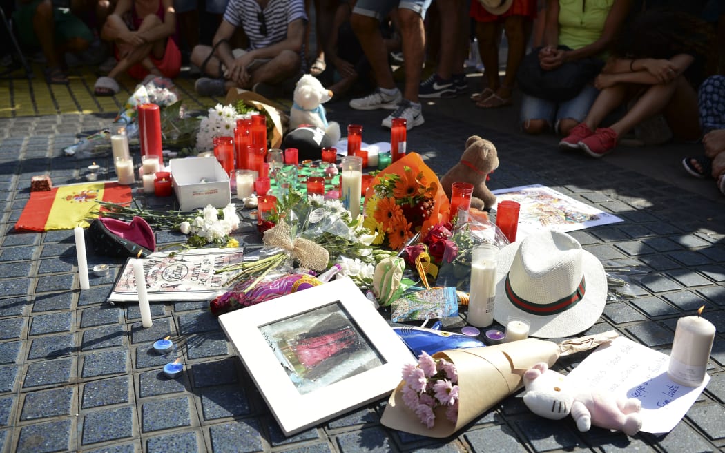 People sit next to flowers, messages, stuffed toys and others items displayed on Las Ramblas boulevard in tribute to the victims of the Barcelona attack, a day after a van drove into pedestrians.