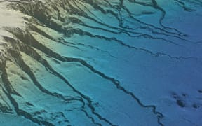 An overview of the underwater landscape showing canyons extending like veins from a rugged plateau and pockmarks in the smooth seafloor surface.