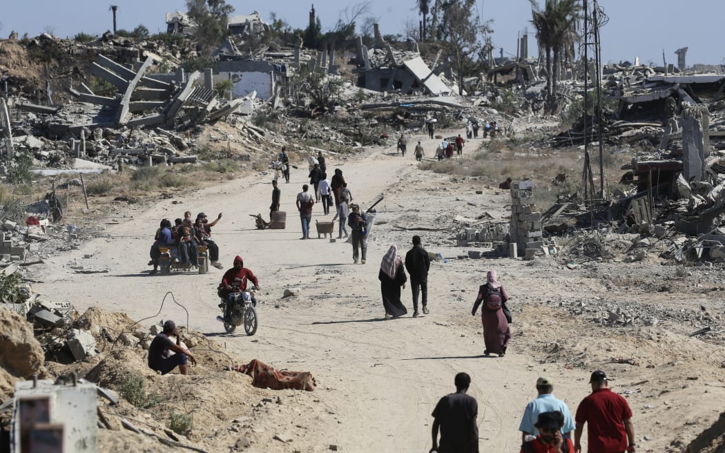 Displaced Palestinians walk past destroyed buildings as they return to their homes in the in al-Zahra area, north of the Nuseirat refugee camp in the central Gaza Strip, on 14 October, 2025, a day after a ceasefire came into effect.