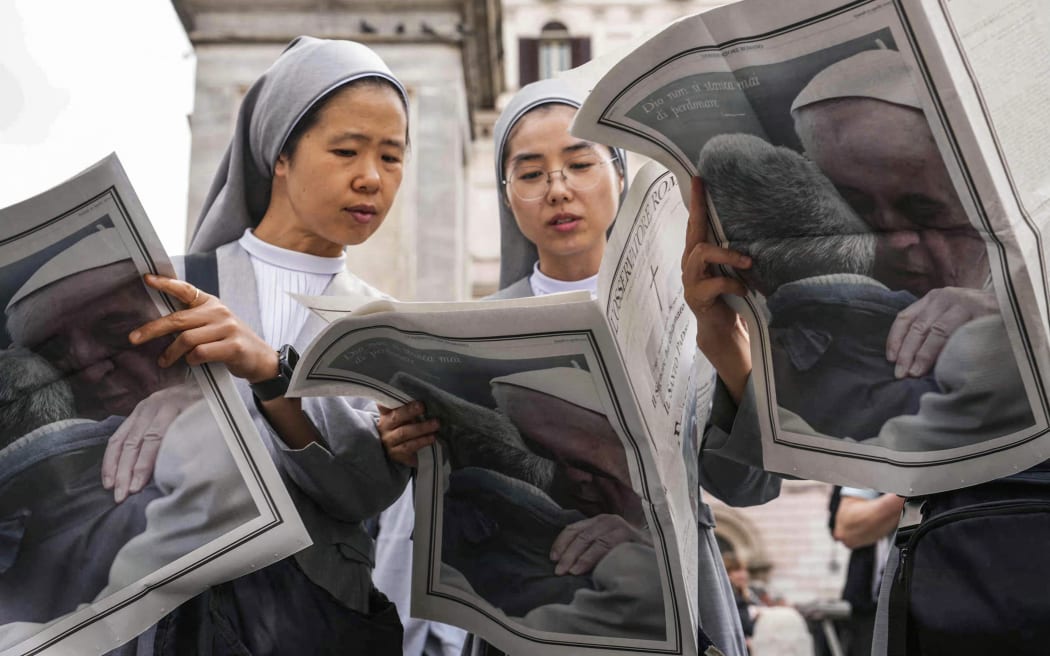 Nuns read through the Osservatore Romano newspaper with Pope Francis on the rear page near Santa Maria Maggiore basilica a day prior to the late Pope's funeral, in Rome on April 25, 2025. The Vatican on April 25, 2025, said over 128,000 people have already paid their respects to Pope Francis, whose body is lying in state in St Peter's Basilica ahead of his funeral set for April 26, 2025. (Photo by Dimitar DILKOFF / AFP)