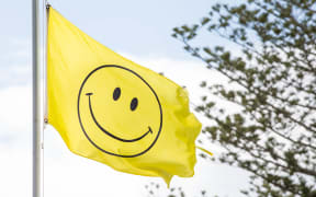 A yellow flag with a smiley face on it flying up a flag pole.