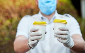 Delivery man in protective mask and gloves, employee hold takeaway cup of coffee. Service quarantine pandemic coronavirus virus Covid-19.