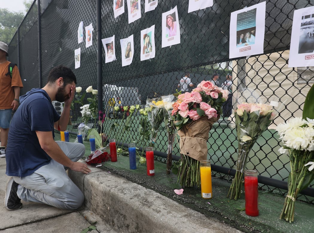 Leo Soto kneels in front of a memorial that includes pictures of missing people on June 25, 2021 in Surfside, Florida