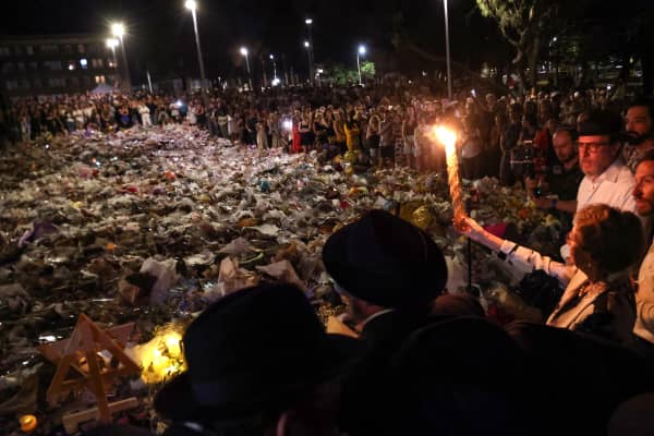 A candle is held up ahead of the seventh candle being lit for the  Jewish festival of Hanukkah as mourners stand next to floral tributes laid out in memory of the victims of a shooting at Bondi Beach, in Sydney, on 20 December, 2025.
