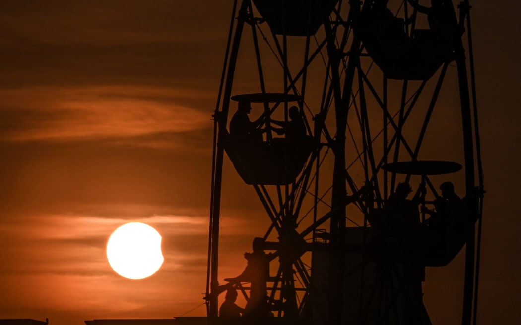 People enjoy a ferris wheel ride as the moon partially obscures the sun during a partial solar eclipse visible from Chennai on 25 October, 2022.