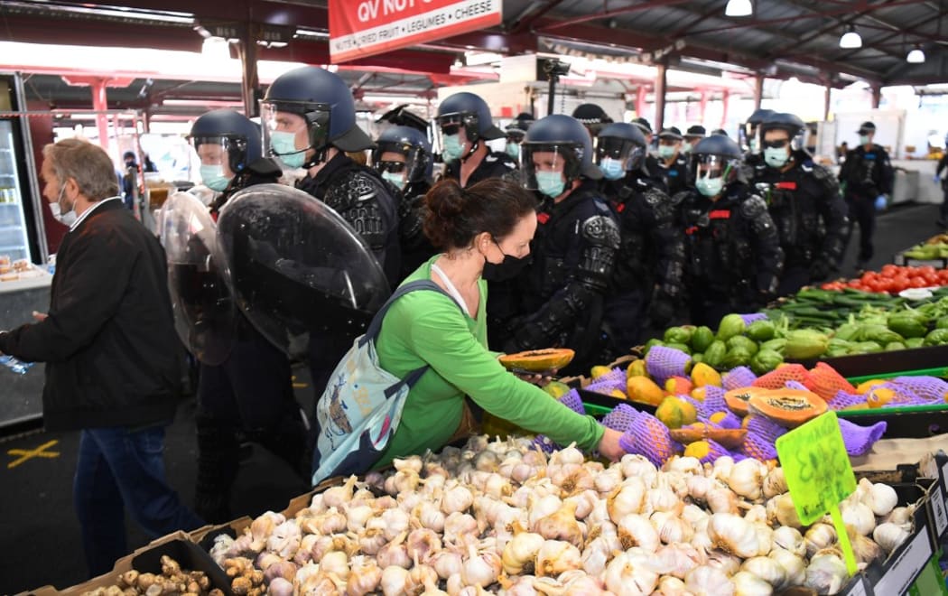 A woman continues to shop for vegetables as riot police clear Melbourne's Queen Victoria Market of anti-lockdown protesters during a rally on September 13, 2020, amid the ongoing COVID-19 coronavirus pandemic.