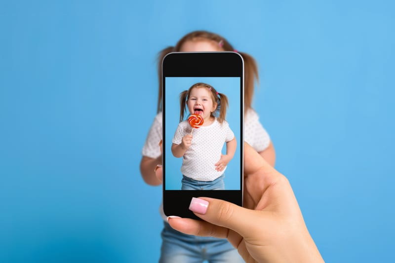 Woman's hand making photo of a little girl with a mobile phone. Selective focus on a mobile phone with a portrait of a girl. Made for social networks