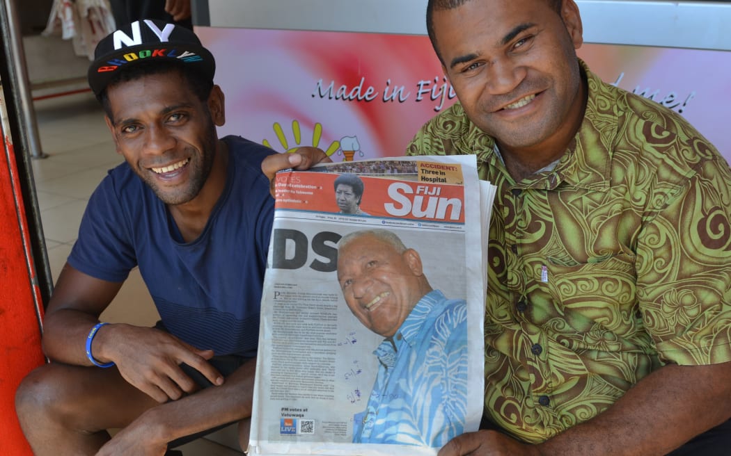 Fiji First Party supporters hold up a local newspaper showing a front page photograph of Frank Bainimarama a day after the Fiji elections.