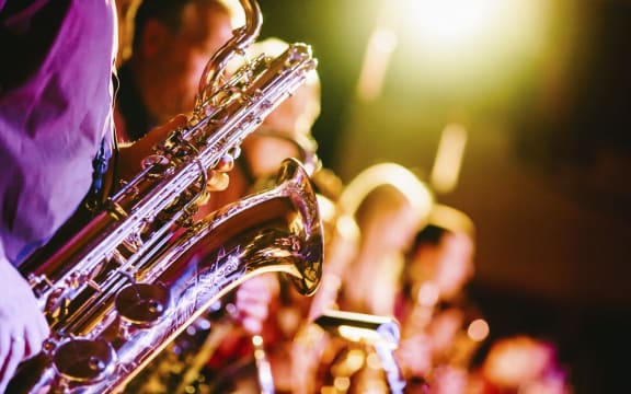 A close-up of a saxophone held by one of the band members during a jazz concert. Original public domain image from Wikimedia Commons