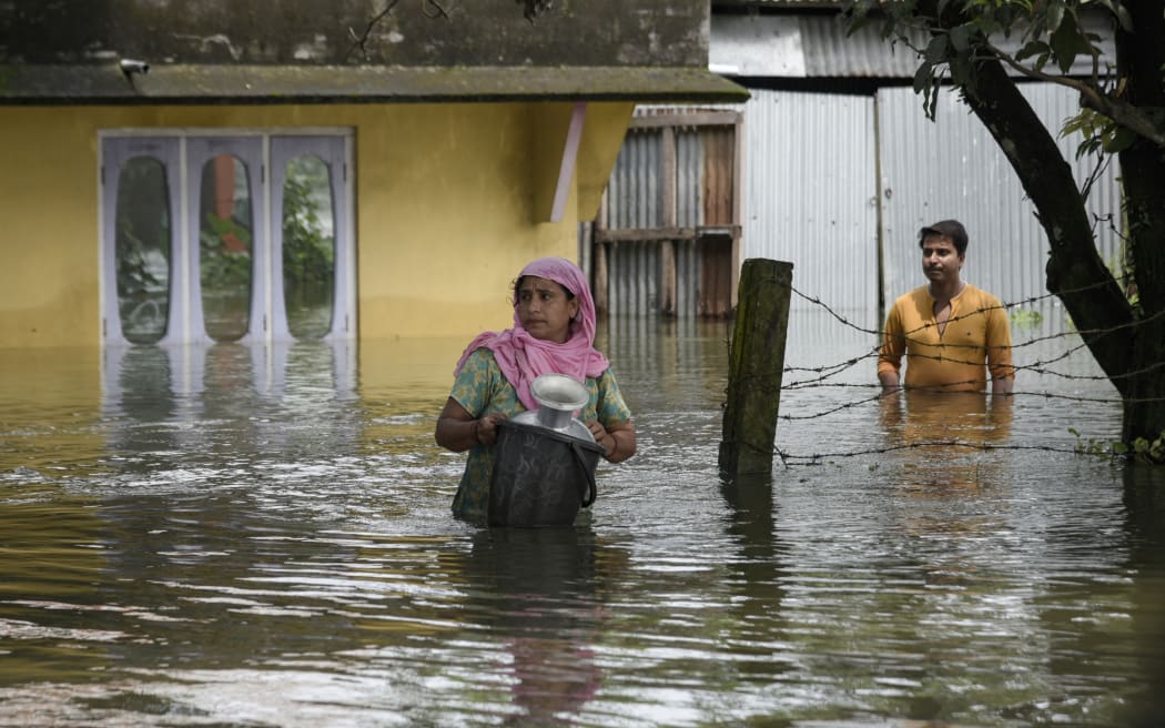 Flood affected people walking in front of their flooded home, at a village in Barpeta, in India's northeastern state of Assam on 20 June, 2022.