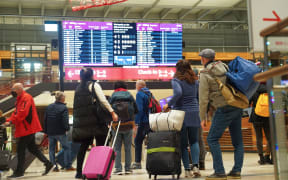 Travellers stand in front of an information board at BER Airport.