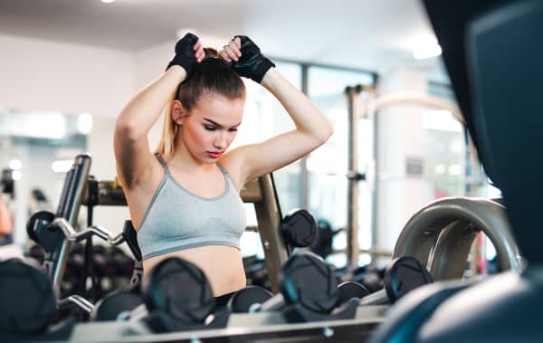 A woman wearing a sports bra, tightening up her ponytail to work out at the gym.