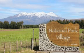 A sign at the entrance to National Park Village that says 'National Park Village', with Mount Ruapēhu visible in the background.