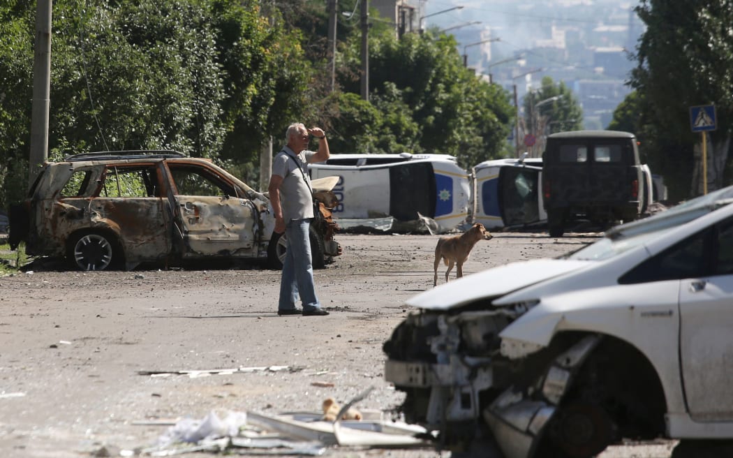 A man stands by a barricade made with destroyed police cars in Lysychansk on 21 June, 2022, as Ukraine says Russian shelling has caused 'catastrophic destruction' in the eastern industrial city, which lies just across a river from Severodonetsk where Russian and Ukrainian troops have been locked in battle for weeks. Regional governor Sergiy Gaiday says that non-stop shelling of Lysychansk on 20 June destroyed 10 residential blocks and a police station, killing at least one person.