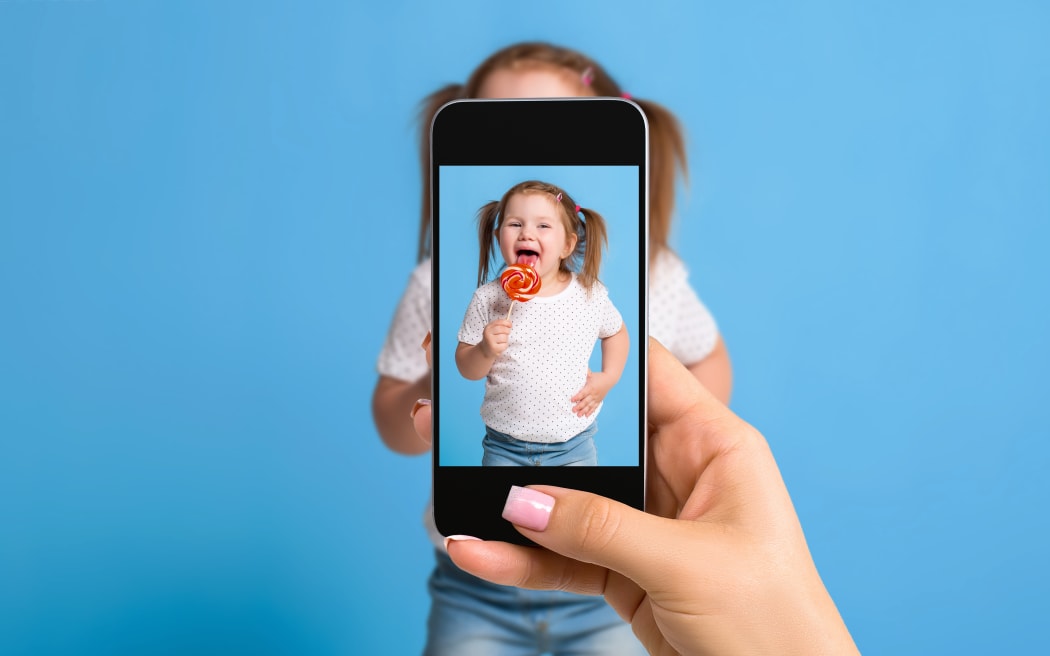 Woman's hand making photo of a little girl with a mobile phone. Selective focus on a mobile phone with a portrait of a girl. Made for social networks