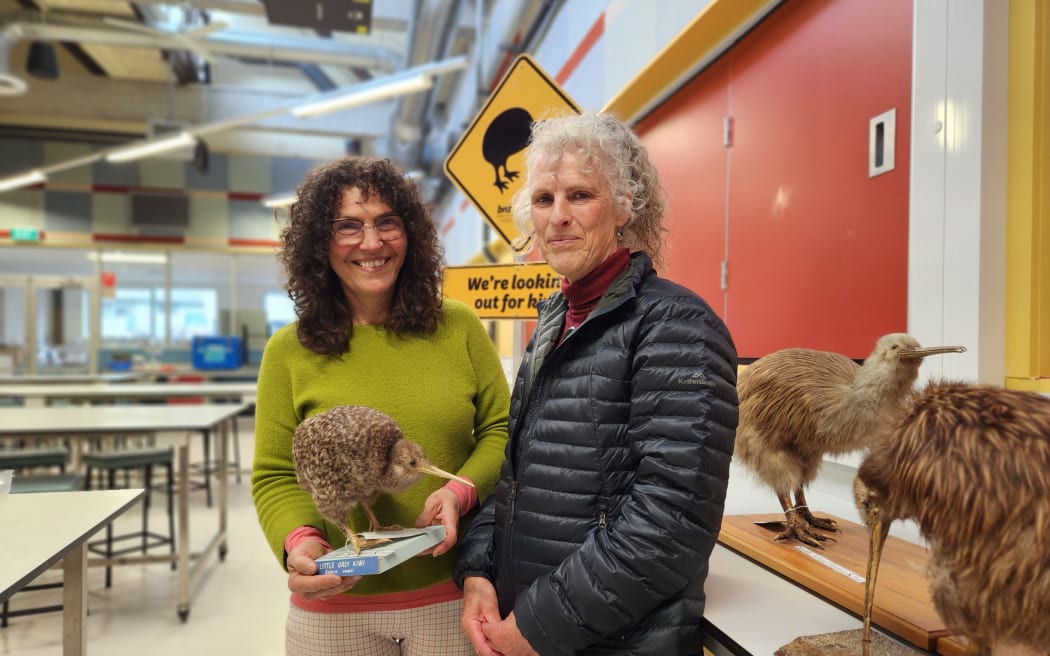 Isabel Castro (L) and Karen Mason standing side by side in a lab at Massey University. Isobel holds a stuffed kiwi.
