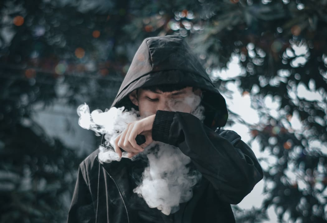 A teenager smokes an e-cigarette.