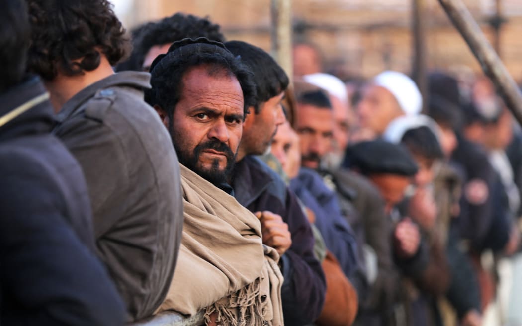 Afghan men stand in queues to receive food aid from a non-governmental organisation (NGO) in Kabul on 25 December, 2022. Several foreign aid groups that day announced they were suspending their operations in Afghanistan after the country's Taliban rulers ordered all NGOs to stop women staff from working.