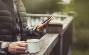 Man drinking coffee using digital tablet on balcony. (Photo by CAIA IMAGE/SCIENCE PHOTO LIBRARY / NEW / Science Photo Library via AFP)