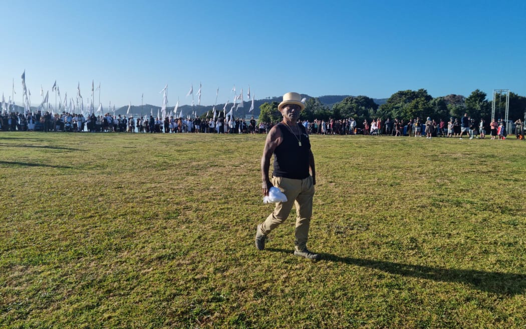 A group of 200 or so people hold up white flags as Tame Iti arrives at Te Whare Runanga on Waitangi Day 2024.