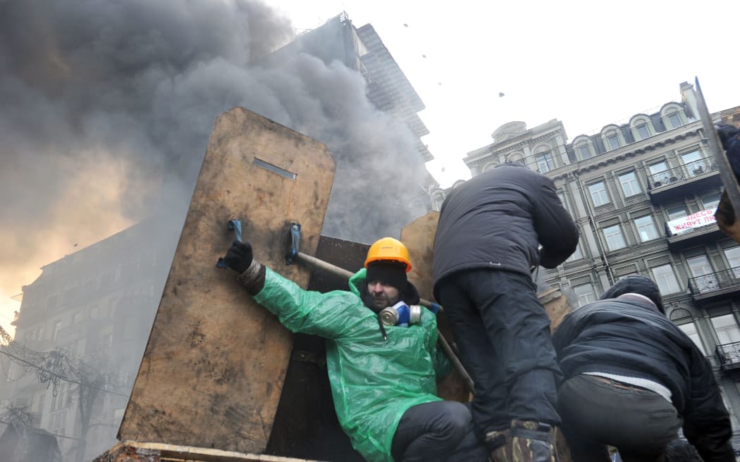 Protesters in Kiev take cover under makeshift shields during a clash with riot police.