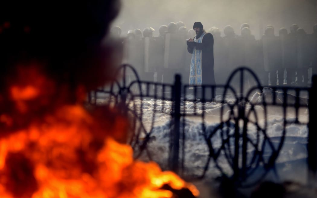 A priest prays in front of riot police in central Kiev.