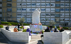 People sit around the statue of Pope John Paul II outside the Gemelli Hospital where Pope Francis is hospitalised with pneumonia, in Rome, on 20 March, 2025.