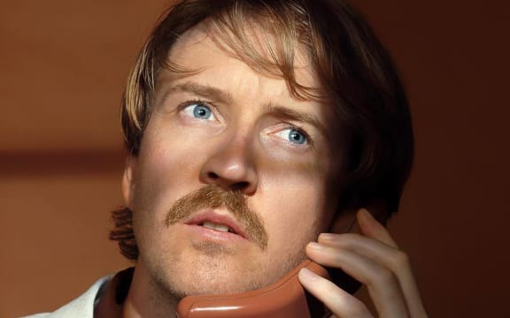 Lawrence Arabia wears a cream suit jacket and holds an old-fashioned phone