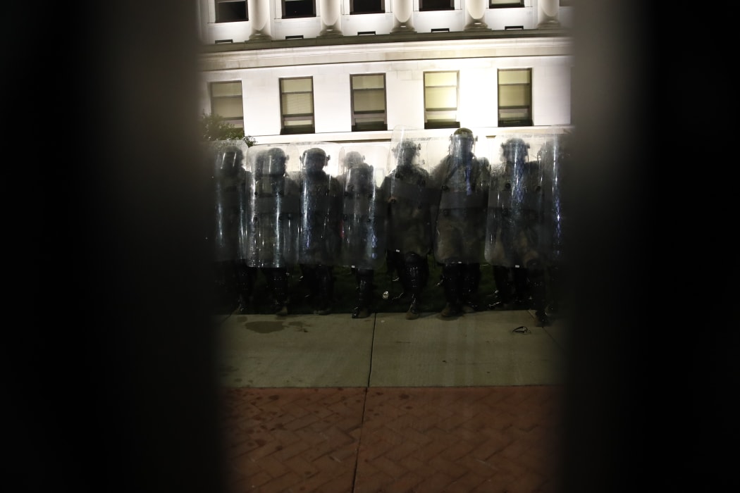 Police in riot gear are seen through the iron fence protecting the County Courthouse during demonstrations against the shooting of Jacob Blake