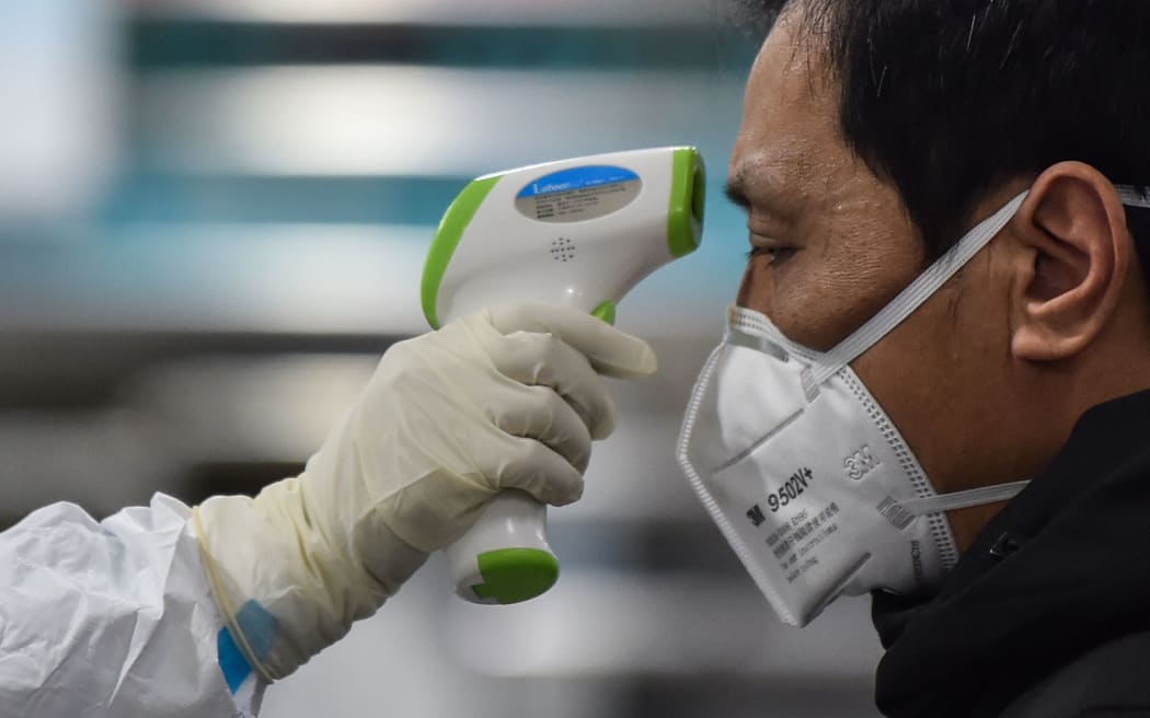 A medical staff member (L) wearing protective clothing to help stop the spread of a deadly virus which began in the city, takes the temperature of a man (R) at the Wuhan Red Cross Hospital in Wuhan on January 25, 2020.