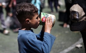 A Palestinian child eats his portion of a hot meal at a free food distribution point at the Nuseirat refugee camp in the central Gaza Strip on April 19, 2025. (Photo by Eyad BABA / AFP)