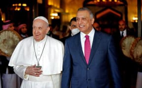 A handout image released by the press office of Iraqi Prime Minister on its Facebook page on March 5, 2021 shows Prime Minister Mustafa al-Kadhemi receiving Pope Francis upon his arrival in the capital Baghdad.