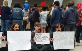 Protestors sit down as shoppers queue to enter Swedish firm H&M's first NZ store.