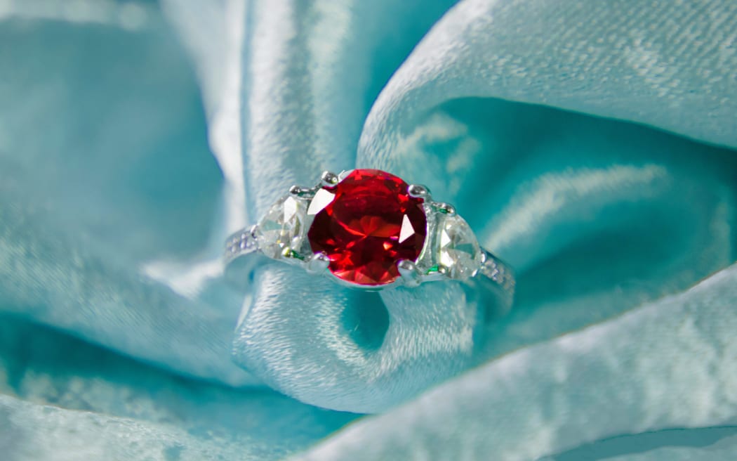 A red ruby gemstone ring on aqua-coloured fabric.