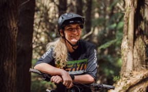 New Zealand mountain bike racer Kate Weatherly leans on her bike, smiling.