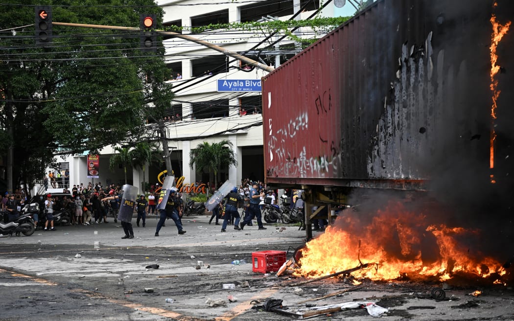 Policemen shield themeselves from rocks thrown by protesters after setting fire to a trailer van near Malacanang Palace in Manila on September 21, 2025. Thousands of Filipinos marched in Manila on September 21 to vent their anger over a ballooning scandal involving bogus flood-control projects believed to have cost taxpayers billions of dollars. (Photo by Ted ALJIBE / AFP)