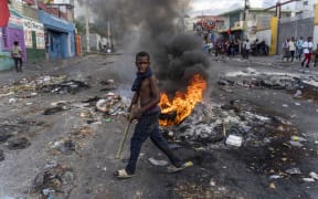 (FILES) In this file photo taken on October 10, 2022 a man walks past a burning barricade during a protest against Haitian Prime Minister Ariel Henry calling for his resignation, in Port-au-Prince, Haiti. - US officials on October 12, 2022 held talks in Haiti on requests for international intervention to combat spiraling insecurity but President Joe Biden's administration indicated reluctance over sending US troops. (Photo by Richard Pierrin / AFP)